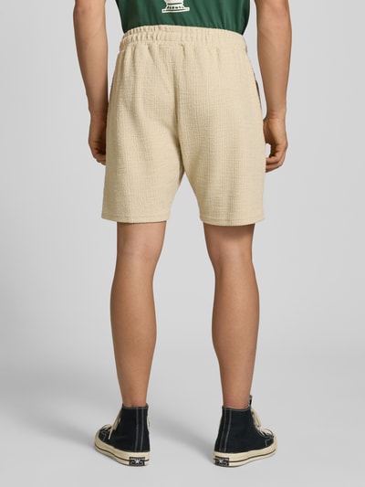 Męski model nosi Shorts mit Label-Patch Modell 'LIBCO' od Pegador, beżowy kolor, materiał z bawełną, prosty krój, widoczne fakturowanie, elastyczny pas, szerokość w rozmiarze M: 38 cm, długość nogawki wewnętrznej: 23 cm, widok całej sylwetki od tyłu.