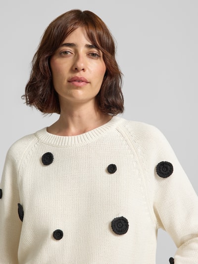Frauenmodel trägt Strickpullover im Allover-Look von Oui aus reiner Baumwolle, cremefarben mit schwarzen Punkten, Nahaufnahme Oberkörper.