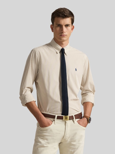 Męski model nosi Slim Fit Freizeithemd aus Baumwoll-Mix od Polo Ralph Lauren, efekt: wzór w paski, krój slim fit, kołnierzyk typu button down, logo, długi rękaw, sportowy mankiet, wykończenie z cieniowanej przędzy, materiał: mieszanka bawełny, kolor beżowy, tekstura gładka, widok na całą sylwetkę z przodu.