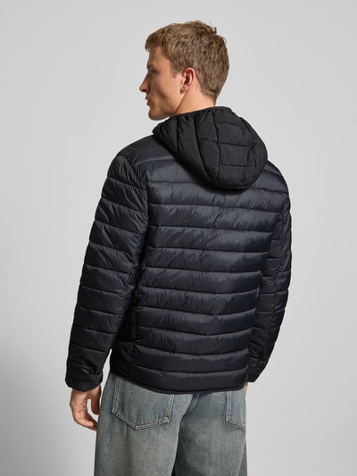 Männermodel trägt Steppjacke mit Kapuze und Logo von CHAMPION in Schwarz, Regular-Fit, Rückansicht, Rückenlänge 71 cm, Schulterbreite 51 cm, Brustweite 61 cm, Ärmellänge 69 cm, mit Reißverschluss und Eingrifftaschen, Ganzkörperansicht Rückansicht.