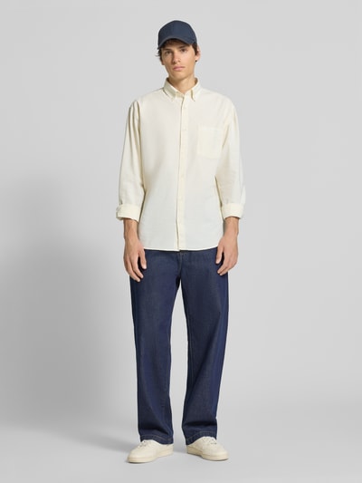 Männermodel trägt Modern Fit Freizeithemd mit Brusttasche Modell 'NORREBRO' von Jack & Jones, Baumwoll-Mix, Ganzkörperansicht von vorne. Das Hemd hat einen Button-Down-Kragen, Knopfleiste, Statement-Stitching an der Brusttasche, Sportmanschetten und abgerundeten Saum, Farbe creme, Struktur glatt. Kombiniert mit blauen Jeans und weißen Sneakern.
