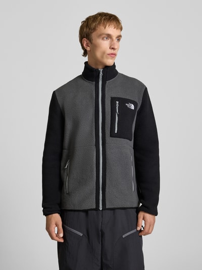 Männermodel trägt Fleecejacke mit Logo-Stitching Modell 'Yumiori' von The North Face in Grau und Schwarz, Gerader-Schnitt, Reißverschluss, Stehkragen, Brusttasche mit Reißverschluss, seitliche Reißverschlusstaschen, Fleece, Ganzkörperansicht von vorne.