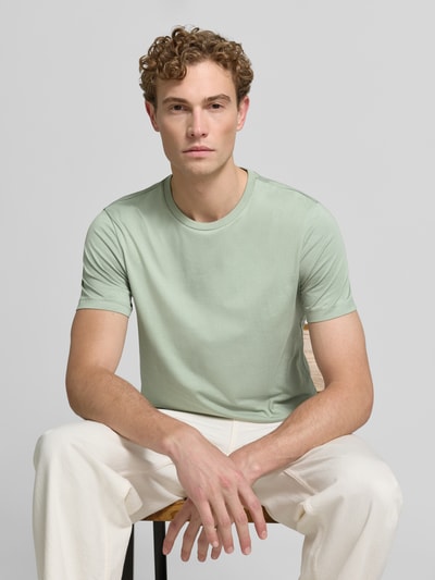 Männermodel trägt T-Shirt aus Baumwolle mit Rundhalsausschnitt von Christian Berg Men, krój slim fit, okrągły dekolt, męski t-shirt, długość tyłu w rozmiarze M: 73 cm, jasny odcień zieleni, prosta faktura, Ganzkörperansicht von vorne