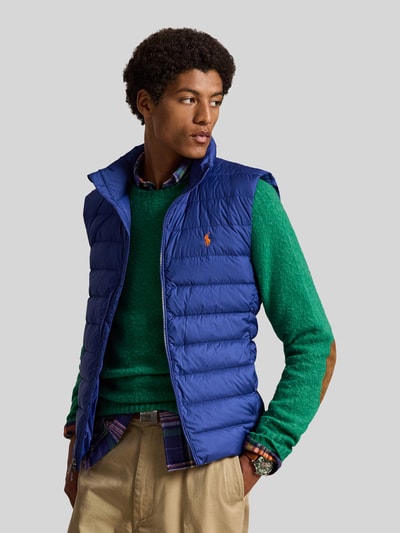 Männermodel trägt Regular Fit Weste mit Logo-Stitching von Polo Ralph Lauren in Blau, kombiniert mit grünem Pullover und beiger Hose, Nahaufnahme Oberkörper.