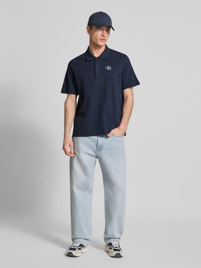 Männermodel trägt Easy Fit Poloshirt mit Polokragen von Calvin Klein Jeans in Dunkelblau, Reine Baumwolle, Label-Stitching, Ganzkörperansicht von vorne. Rückenlänge bei Größe M: 71 cm.