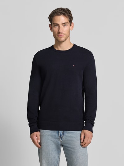 Männermodel trägt Regular Fit Pullover aus reiner Baumwolle von Tommy Hilfiger in Dunkelblau, kombiniert mit Jeans, Ganzkörperansicht von vorne. Herren Pullover von Tommy Hilfiger.