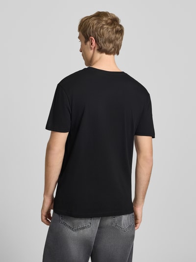 Männermodel trägt T-Shirt mit Logo und Rundhalsausschnitt von Alpha Industries in Schwarz, reine Baumwolle, Regular Fit, Rückansicht, Ganzkörperansicht.