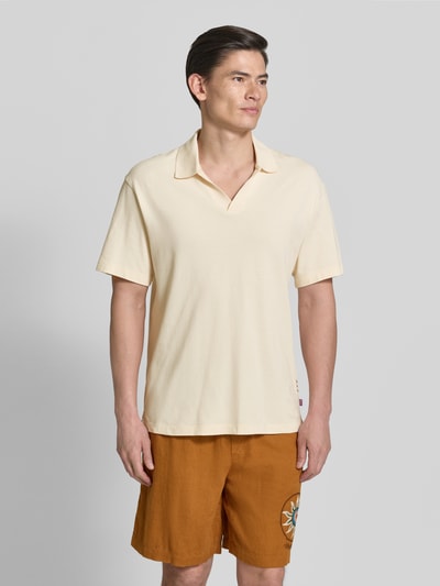 Męski model nosi Relaxed Fit Poloshirt in Pique-Optik od Scotch & Soda, bawełna, krój relaxed fit, beżowy, krótki rękaw, piqué, widok całej sylwetki z przodu.