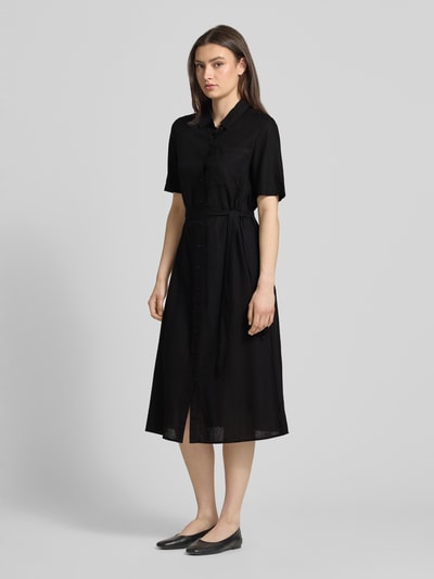 Modelka kobieca nosi czarne, jednokolorowe midi Freizeitkleid z V-dekoltem, krótkim rękawem, kieszenią na piersi z flammgarnu, wykonane z mieszanki wiskozy i lnu Figurumsielendes Freizeitkleid aus Viskose-Leinen-Mix Modell 'PIA' od Pieces, widok całopostaciowy z przodu.