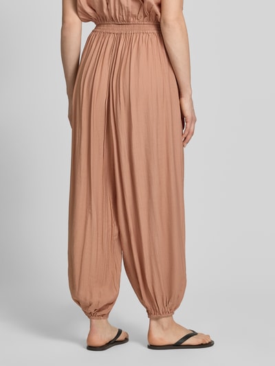 Vrouwenmodel draagt harembroek met zij-steekzakken van Style Icon Collection in lichtbruine kleur, los model, elastische band en zoom, ganzekörperaanzicht achteraan.