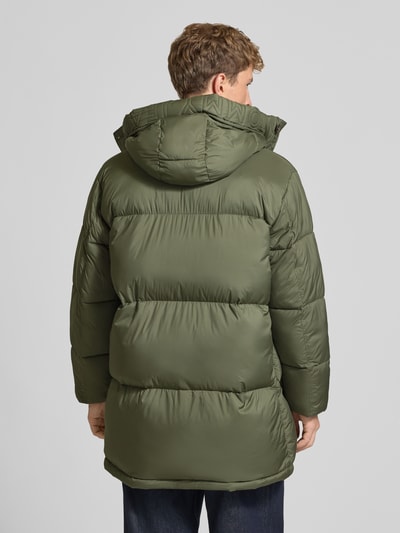 Männermodel trägt Parka mit Logo-Patch Modell 'WORKWEAR' von Tommy Jeans in matt-olivgrün, Struktur, Longline, Ganzkörperansicht Rückansicht.