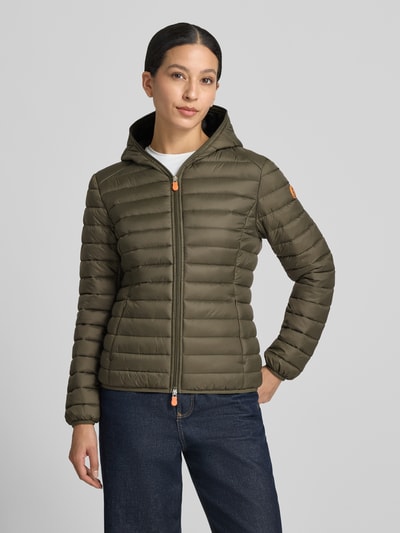 Frauenmodel trägt Steppjacke mit Zweiwege-Reißverschluss Modell 'DAISY' von Save The Duck, olivgrün, glatte Oberfläche, Ganzkörperansicht von vorne, Damen Steppjacke Slim Fit mit Kapuze, Reißverschlusstaschen, Rückenlänge 57 cm, Schulterbreite 44 cm, Brustweite 48 cm, Ärmellänge 60 cm.