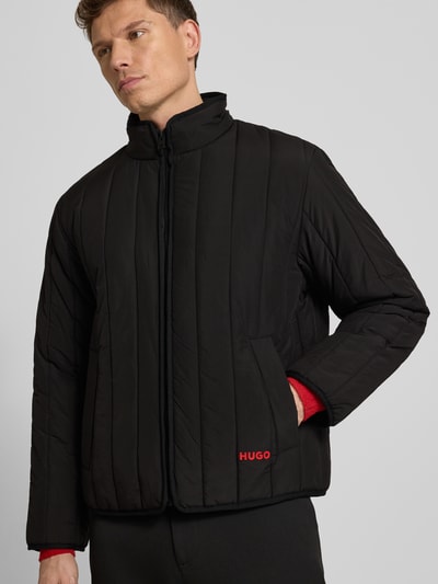 Männermodel trägt Regular Fit Steppjacke mit Stehkragen Modell 'BRENOTO' von HUGO, Optik: Unifarben, Label Print, Langarm, seitliche Eingrifftaschen, verdeckter Reißverschluss, Ganzkörperansicht von vorne.