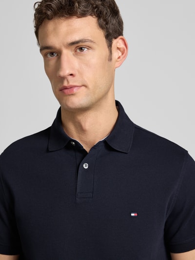 Männermodel draagt Regular Fit Poloshirt met logo-stitching van Tommy Hilfiger, donkerblauwe kleur, katoen-elastaanmix, nahaufnahme bovenlichaam.