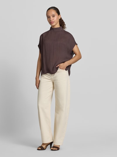 Frauenmodel trägt Regular Fit Bluse aus reiner Viskose Modell 'Lisea' von Someday, strukturierte Oberfläche, Stehkragen, kurzärmelig, dunkles Braun, kombiniert mit heller Hose, Ganzkörperansicht von vorne.