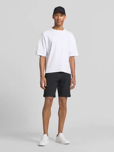 Männermodel trägt Regular Fit Chinoshorts aus Baumwoll-Mix von Tom Tailor Denim in Bi-Color Optik, mit Gürtel und seitlichen Eingrifftaschen, Ganzkörperansicht von vorne.