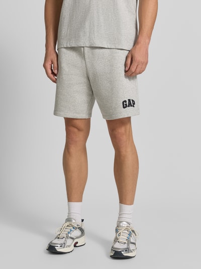 Männermodel trägt Straight Fit Shorts mit Logo-Stitching Modell 'Heritage' von GAP in Hellgrau, Baumwoll-Mix, Ganzkörperansicht von vorne.