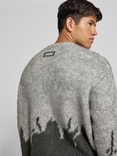 Männermodel trägt Strickpullover mit gerippten Abschlüssen von ANOTHER COTTON LAB, graue Töne und weiche Textur, Ganzkörperansicht Rückansicht. Elastischer Material-Mix mit Lanawoll-Anteil, gerader Schnitt, Rundhalsausschnitt, überschnittene Ärmel, gerippte Abschlüsse.