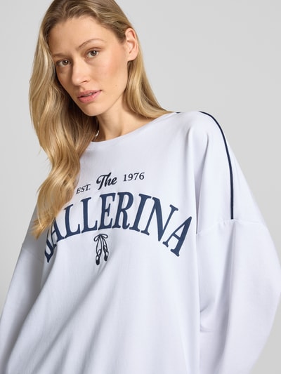 Frauenmodel trägt Oversized Sweatshirt aus Baumwoll-Mix Modell 'JAMIE' von Vero Moda in Weiß mit Motiv-Print, Kontraststreifen und Rundhals, Nahaufnahme Oberkörper.