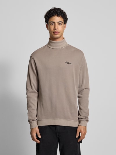 Męski model nosi Sweter z golfem w efekt prążkowania z wyhaftowanym logo od Pegador, bawełna, krój relaxed fit, długość tyłu 70 cm, długość rękawów 70 cm, kolor beżowy, gładka tekstura, całkowity widok z przodu.