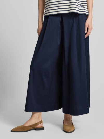 Vrouwenmodel draagt Wide Fit Stoffhose mit Bundfalten van Christian Berg Woman in donkerblauw, gemaakt van pure katoen, wide fit, verkorte pasvorm, elastische tailleband, zichtbare plooien. Detailopname benen.