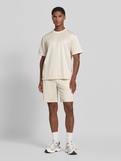 Männermodel trägt Regular Fit Sweatshorts mit Monogramm-Logo-Print von Lacoste in Creme, dezente Textur, Herren Sweatshorts, Ganzkörperansicht von vorne.