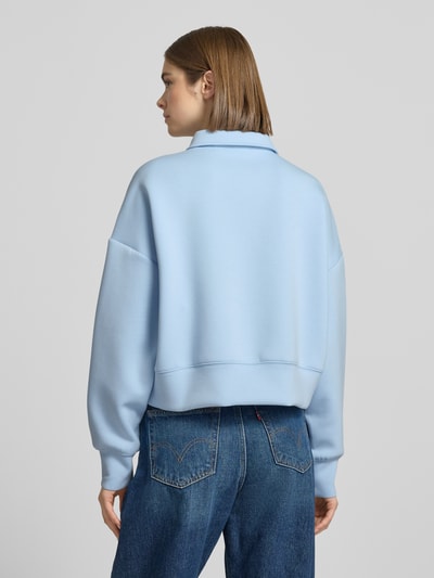 Frauenmodel trägt Cropped Pullover mit Viskose-Anteil von Guess Jeans in Hellblau mit Polo-Kragen und Logo-Stitching, Ganzkörperansicht Rückansicht.