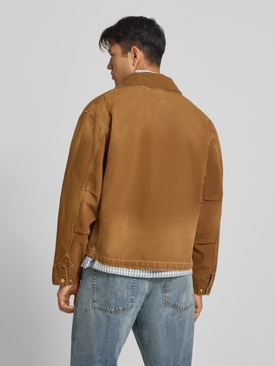 Männermodel trägt Jacke mit Reißverschluss und Label-Detail Modell 'Dearborn' von Carhartt Work In Progress in Braun, Ganzkörperansicht Rückansicht. Produkt besteht aus reiner Baumwolle mit Umlegekragen, sichtbarer Struktur und entspanntem Schnitt.