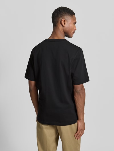 Männermodel trägt Regular Fit T-Shirt mit Logo-Print Modell 'Bobby' von Wood Wood aus reiner Baumwolle, schwarze Farbe, Ganzkörperansicht Rückansicht.