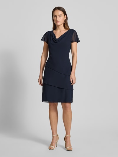 Modelka kobieca nosi tailliertes Cocktailkleid mit Volants od Christian Berg Cocktail, granatowa tkanina, długość do kolan, widok z przodu, całopostaciowy.