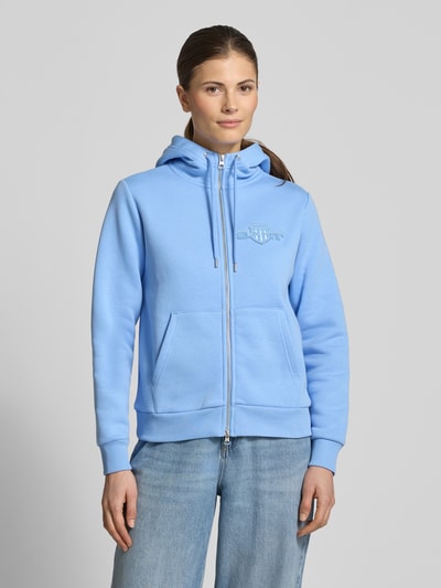 Frauenmodel trägt Sweatjacke mit Zweiwege-Reißverschluss und Label-Stitching von Gant, hellblau, Kapuze, Känguru-Tasche, Ganzkörperansicht von vorne