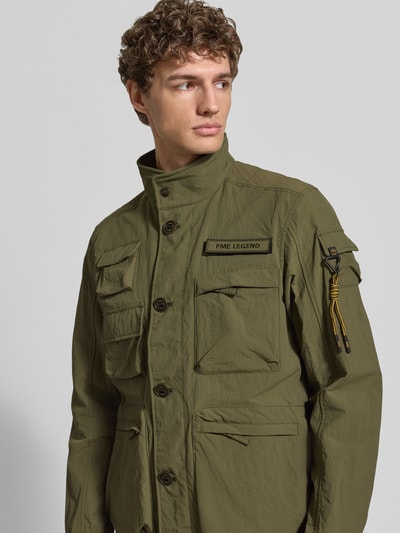 Mężczyzna model nosi Jacke mit Stehkragen und Cargotaschen Modell 'CARGOYET' von PME Legend w kolorze oliwkowym, krój regular fit, tekstura lekko marszczona, widoczne kieszenie cargo, detal z logo, zapięcie na guziki, widok na górną część ciała z przodu. Szerokość w rozmiarze M: 58 cm, długość tyłu: 72 cm, szerokość ramion: 47 cm, długość rękawa: 67 cm.
