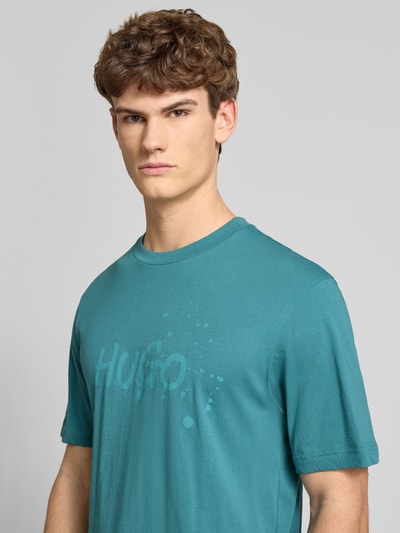 Männermodel trägt Regular Fit T-Shirt aus reiner Baumwolle Modell 'NIEROFIX_U261' von HUGO in Unifarbe mit Label Stitching und Motiv-Print, Nahaufnahme Oberkörper.