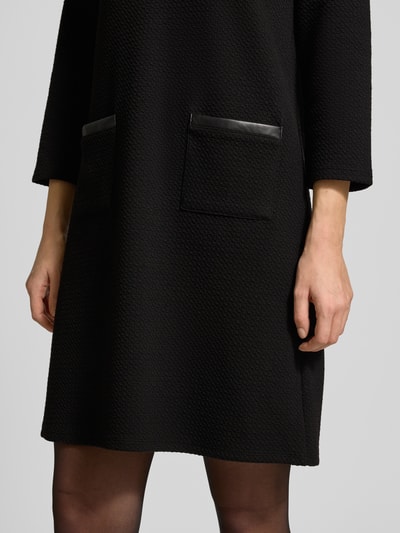Frauenmodel trägt Minikleid mit 3/4-Ärmel von More & More, Material-Mix mit Baumwoll-Anteil, taillierter Schnitt, Eingrifftaschen, Nahaufnahme Unterkörper.