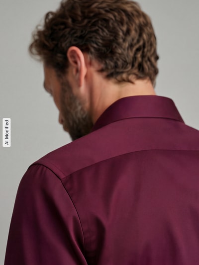 Männermodel trägt Slim Fit Businesshemd aus reiner Baumwolle von Seidensticker in dunklem Bordeauxrot, glatte Struktur, Ganzkörperansicht Rückansicht. Herren Businesshemd von Seidensticker.