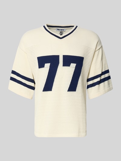 Produktfoto, Strick-Trikot mit Jacquard Muster von REVIEW, prosty krój, dekolt w serek, rękaw o dł. 1/2, perforowanie, długość tyłu w rozmiarze M: 69 cm. Jasnokremowa dzianina z granatowymi paskami i żakardowym wzorem z przodu, faktura ażurowa.