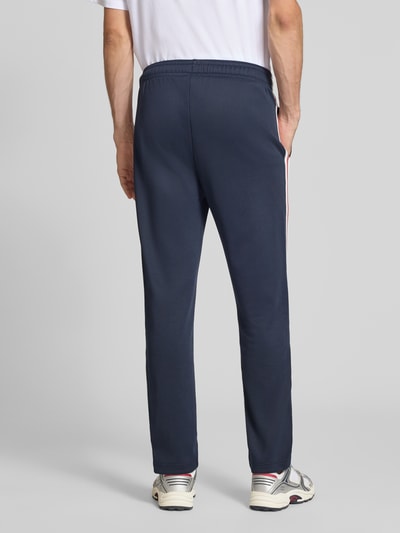 Männermodel trägt Sweatpants mit Bordüre von Champion in Dunkelblau, Material-Mix, gerader Schnitt, Elastikbund, Ganzkörperansicht Rückansicht.