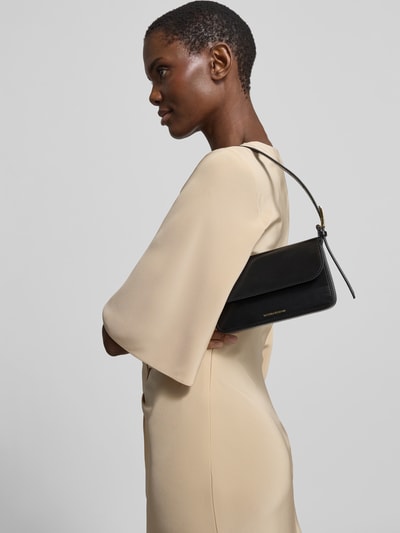 Frauenmodel trägt Pocket Bag mit Überschlag von Victoria Beckham in Schwarz mit Ziernähte, Label-Print in metallic, Hauptfach, Magnetverschluss, verstellbarer Schulterriemen, Ganzkörperansicht von vorne.