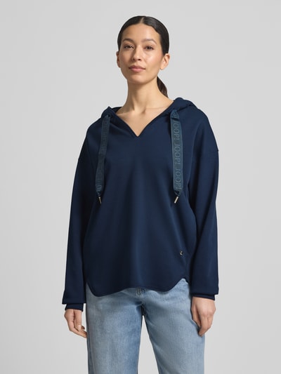 Frauenmodel trägt Oversized Hoodie aus Baumwoll-Mix Modell 'Tristani' von JOOP! in Dunkelblau, mit Kapuze, Tunnelzug und Eingrifftaschen, Ganzkörperansicht von vorne.