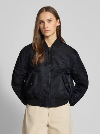 Frauenmodel trägt Bomberjacke mit Stehkragen und Reißverschluss Modell 'SCOUT' von Levi's®, Schwarz, glatte Textur, Nahaufnahme Oberkörper. Regular Fit, Pattentaschen, Rückenlänge 50 cm, Schulterbreite 42 cm, Brustweite 40 cm, Ärmellänge 59 cm.