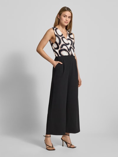 Frauenmodel trägt Jumpsuit mit Eingrifftaschen Modell 'Bi44lina' von ZABAIONE, Schwarz mit gemustertem Oberteil, V-Ausschnitt, Material-Mix mit Stretch-Anteil, weite Beine, Ganzkörperansicht von vorne.