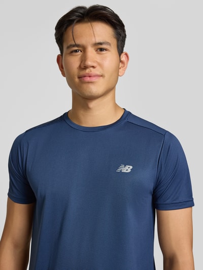 Männermodel trägt Funktionsshirt mit Rundhalsausschnitt und Logo von New Balance in Dunkelblau, glatte Oberfläche, Nahaufnahme Oberkörper, Regular Fit, Rückenlänge bei Größe M 69 cm.