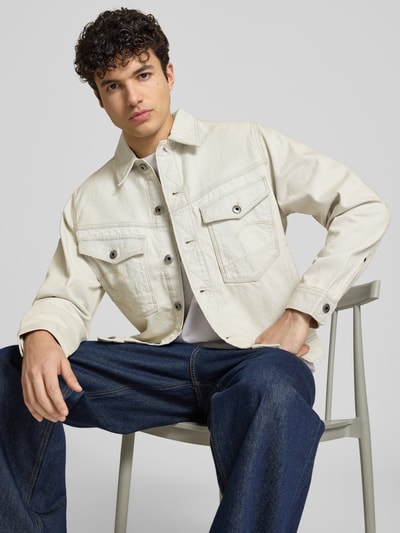 Męski model nosi Jeansjacke mit Brusttaschen Modell 'Dakota' von G-Star Raw w kolorze jasnokremowym, czysta bawełna, krój relaxed fit, kołnierz, kieszenie na piersi, długość tyłu w rozmiarze M: 63 cm, szerokość ramion w rozmiarze M: 47 cm, szerokość w rozmiarze M: 58 cm, długość rękawa w rozmiarze M: 65 cm, tekstura gładka, przód, zbliżenie na górną część ciała.