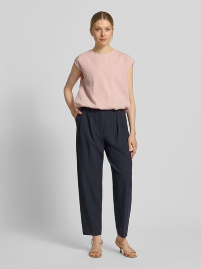Frauenmodel trägt Bluse mit Rundhalsausschnitt und Kappärmeln von Jake*s Collection in zartem Rosa, kombiniert mit dunkelblauer Stoffhose, gerade geschnittener Stil, marmorierte Sandalen, glatte Stofftextur, Ganzkörperansicht von vorne.