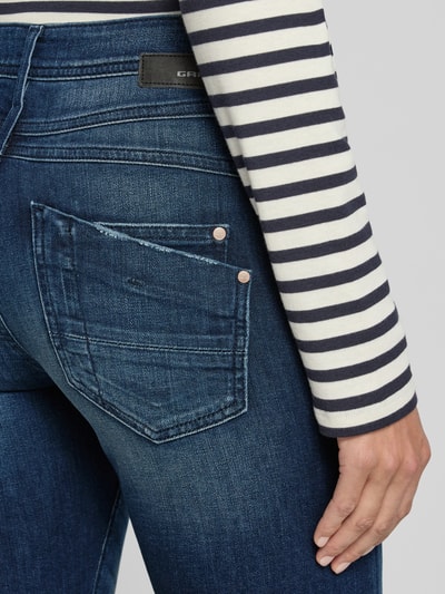 Frauenmodel trägt Straight Fit Jeans aus Baumwoll-Mix Modell 'AMELIE' von GANG, mittelblaue Denim mit auffälliger Gesäßtasche, Nahaufnahme Oberkörper, Damen Wide & Loose Fit Jeans von GANG.