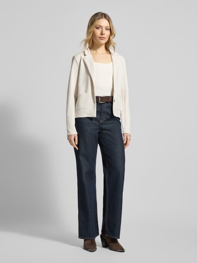 Kobieta nosi Sweatblazer mit Taschen und Revers von Christian Berg Woman, mieszanka materiałów z dodatkiem modalu, krój regular fit, kieszenie, kołnierz z połami, zapięcie na guzik, jasnobeżowy żakiet, granatowe spodnie, widok całej sylwetki z przodu.