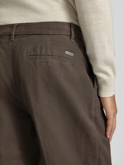 Männermodel trägt spodnie z zakładkami w pasie z kieszeniami z tyłu Bundfaltenhose mit Gesäßtaschen od Armani Exchange, krój regular fit, detal z logo, ciemnobrązowy materiał, Szerokość w rozmiarze 32: 44 cm, Długość wewnętrzna nogawki w rozmiarze 32: 80 cm, Ganzkörperansicht Rückansicht.