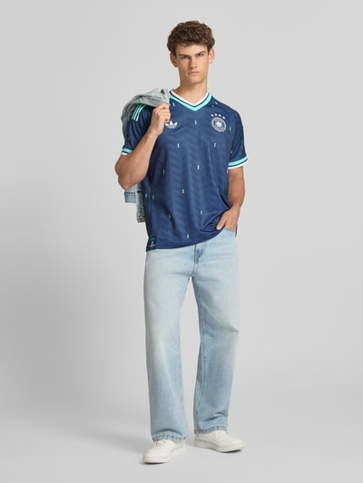 Männermodel trägt DFB Auswärtstrikot Deutschland 2026 von adidas Sportswear, Mehrfarbig, Passform: Slim-Fit, Applikation: Logo-Details, Ausschnitt: V-Ausschnitt, Ärmelform: Kurzarm, Ganzkörperansicht von vorne.