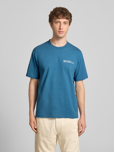 Männermodel trägt Relaxed Fit T-Shirt aus reiner Baumwolle mit Motiv-Print von Marc O'Polo Denim in Blau, Optik: Unifarben, Passform: Relaxed-Fit, Applikation: Motiv-Print, Rundhals, Ärmelform: Kurzarm, Ganzkörperansicht von vorne.