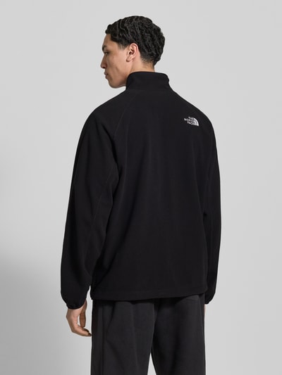 Männermodel trägt Fleecejacke mit Label-Stitching von The North Face in schwarz, regular fit, Stehkragen, Reißverschluss, Rückenlänge 69 cm, Ärmellänge 69 cm, Ganzkörperansicht Rückansicht